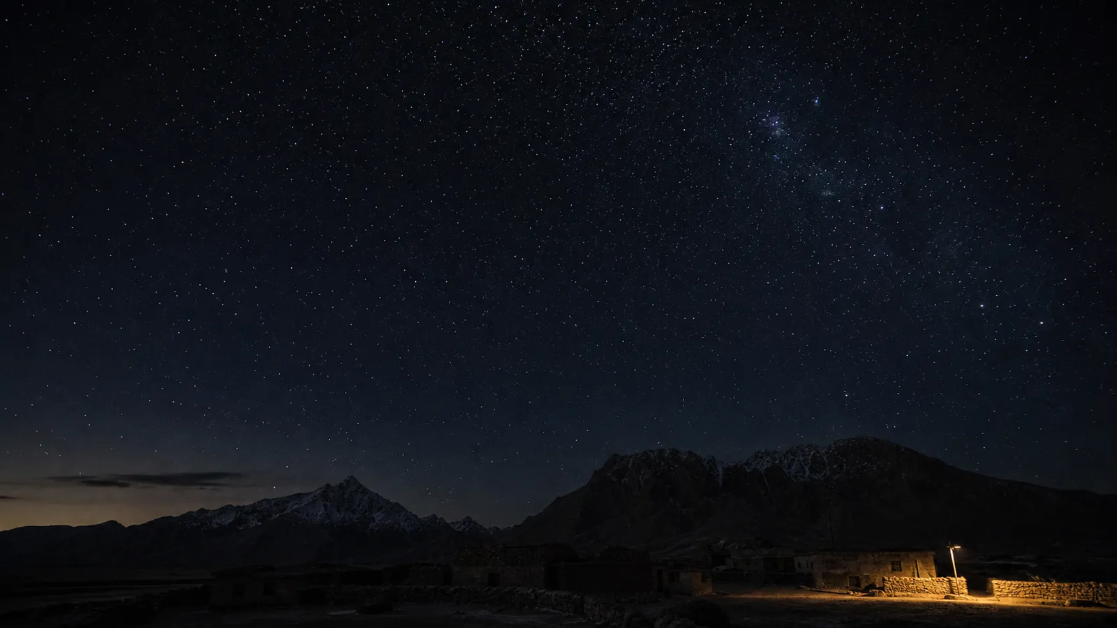 A single shielded village lamp points downward beneath an immense dark mountain sky.