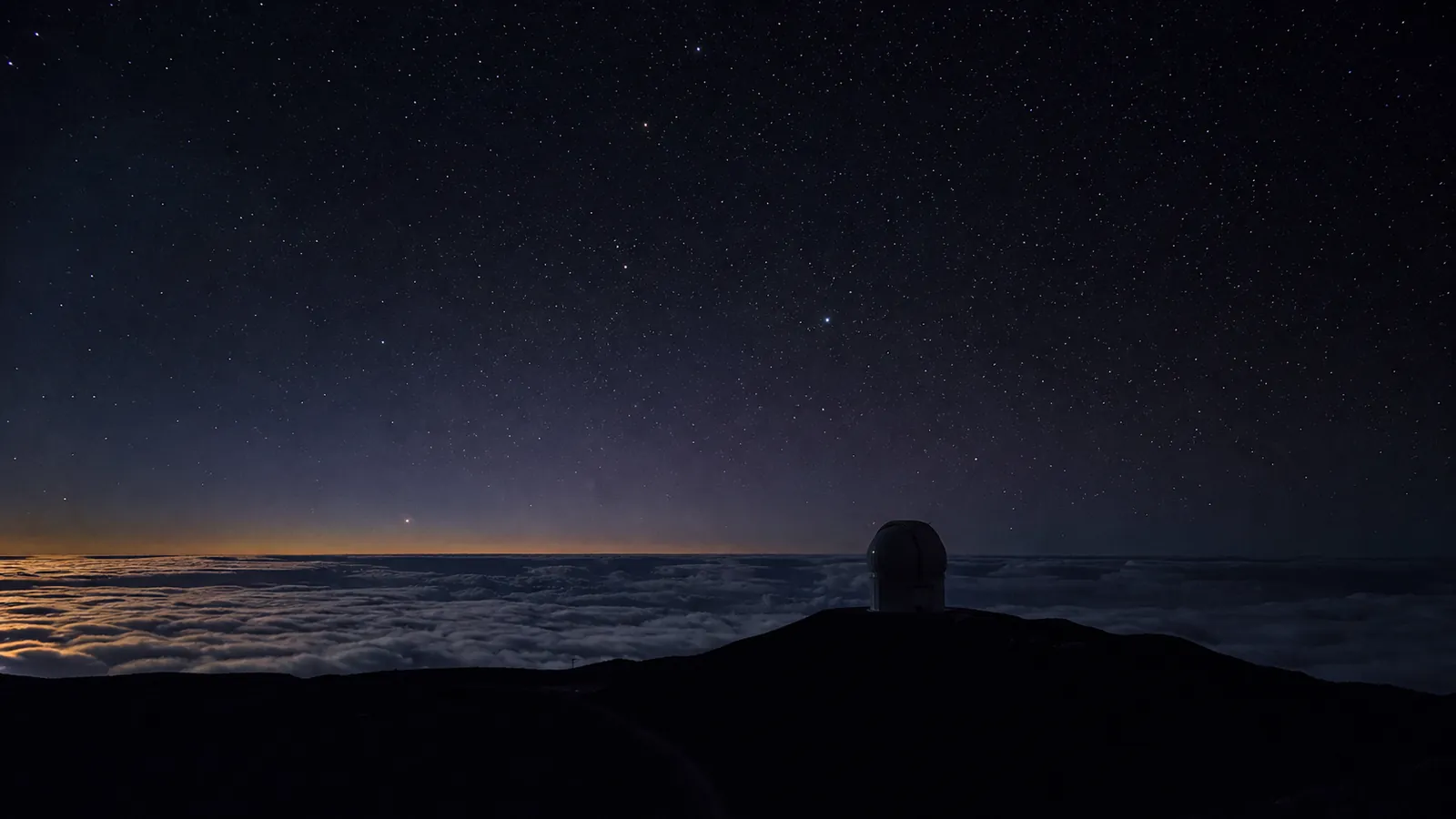 A Haleakalā observatory dome beneath stars above a moonlit sea of clouds.