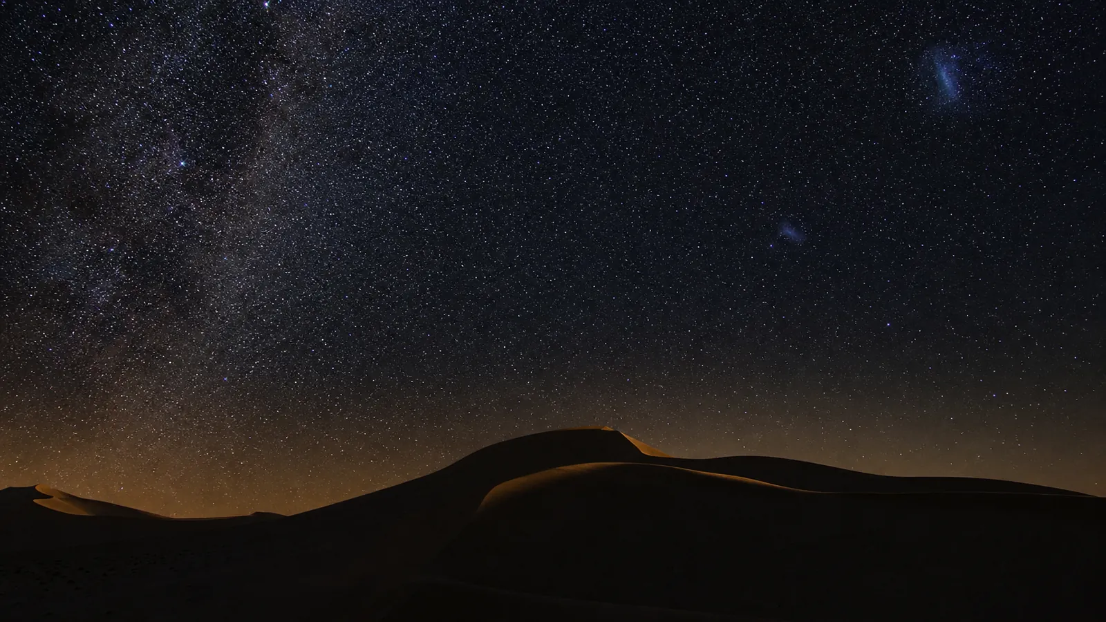 Southern stars and the Magellanic Clouds above silhouetted NamibRand dunes.